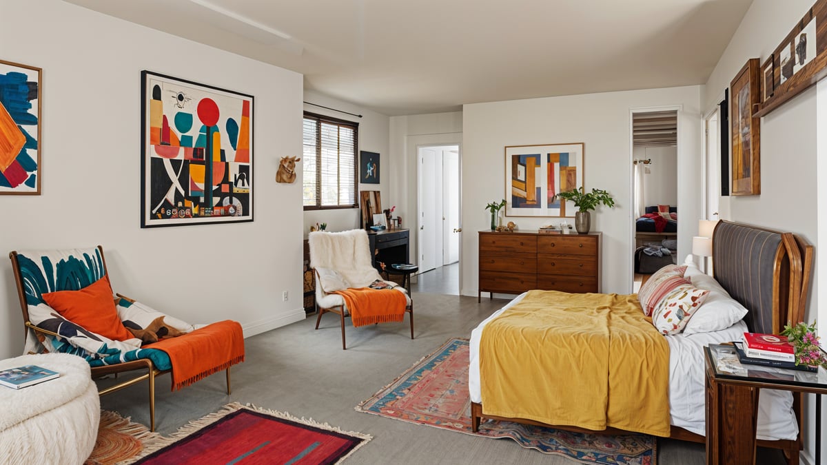 Eclectic bedroom with a large bed, a chair, and a rug. The room features a white color scheme with a touch of orange and red accents.